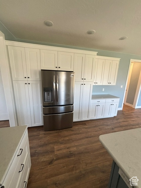 Kitchen with stainless steel refrigerator with ice dispenser, dark wood-style floors, white cabinetry, light countertops, and baseboards