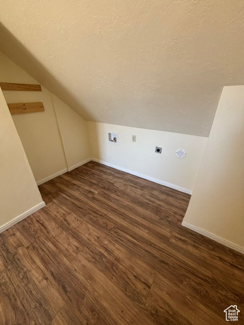 Bonus room featuring a textured ceiling, lofted ceiling, dark wood-style floors, and baseboards