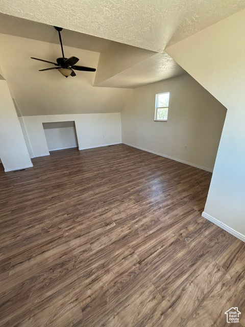 Additional living space with ceiling fan, lofted ceiling, a textured ceiling, baseboards, and dark wood-style floors