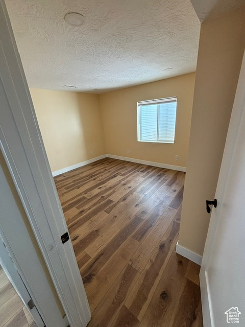 Empty room with light wood-type flooring, a textured ceiling, and baseboards
