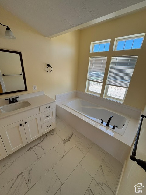 Bathroom featuring marble finish floors, a garden tub, and vanity