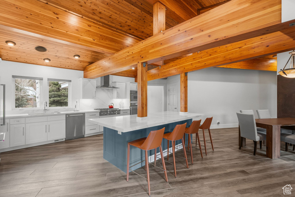 Kitchen featuring a center island, a sink, stainless steel appliances, white cabinets, and wall chimney range hood