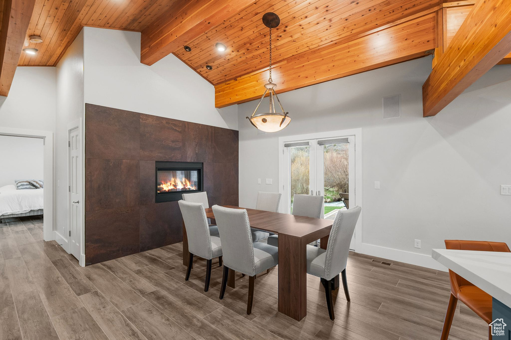 Dining space featuring wood finished floors, beam ceiling, high vaulted ceiling, visible vents, and a tiled fireplace