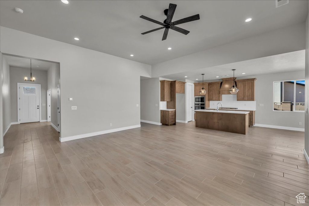 Unfurnished living room featuring baseboards, light wood finished floors, recessed lighting, and ceiling fan with notable chandelier