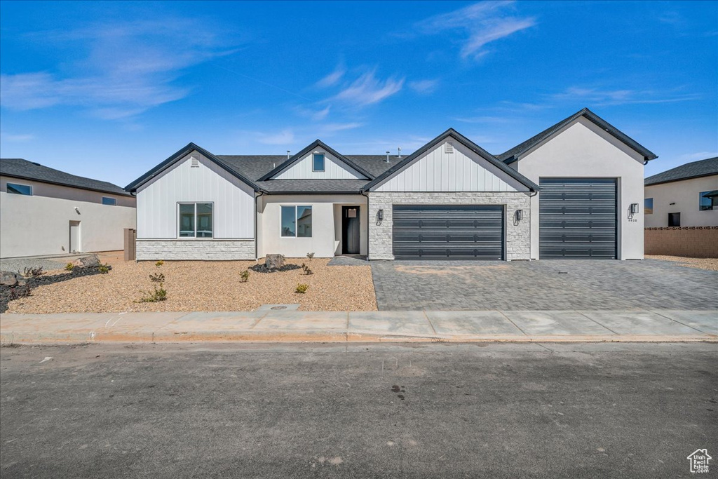 Modern farmhouse with stone siding, a garage, and decorative driveway