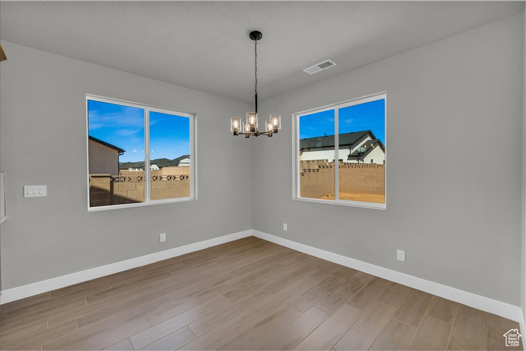 Unfurnished room with a chandelier, visible vents, wood finished floors, and baseboards
