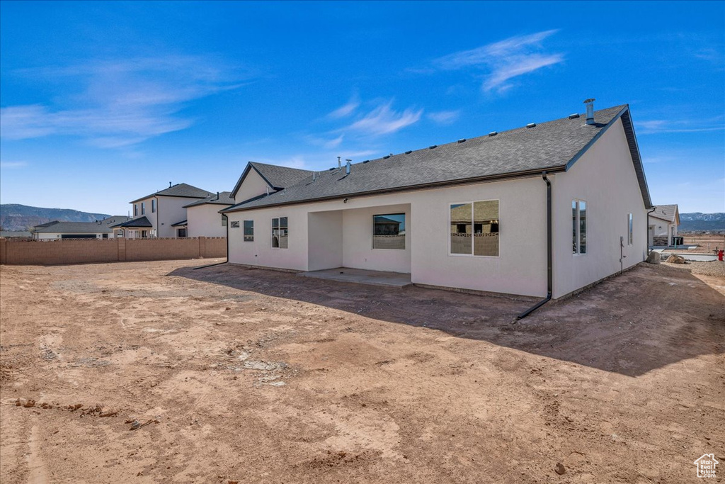 Back of house featuring a shingled roof, a mountain view, stucco siding, and fence