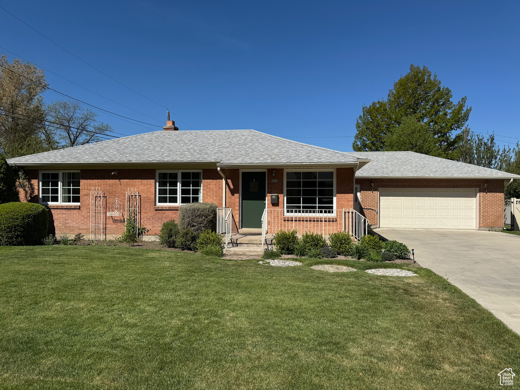 Ranch-style home with a garage, a front lawn, brick siding, and driveway