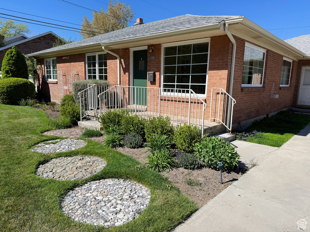 View of front facade with a front yard, roof with shingles, and brick siding
