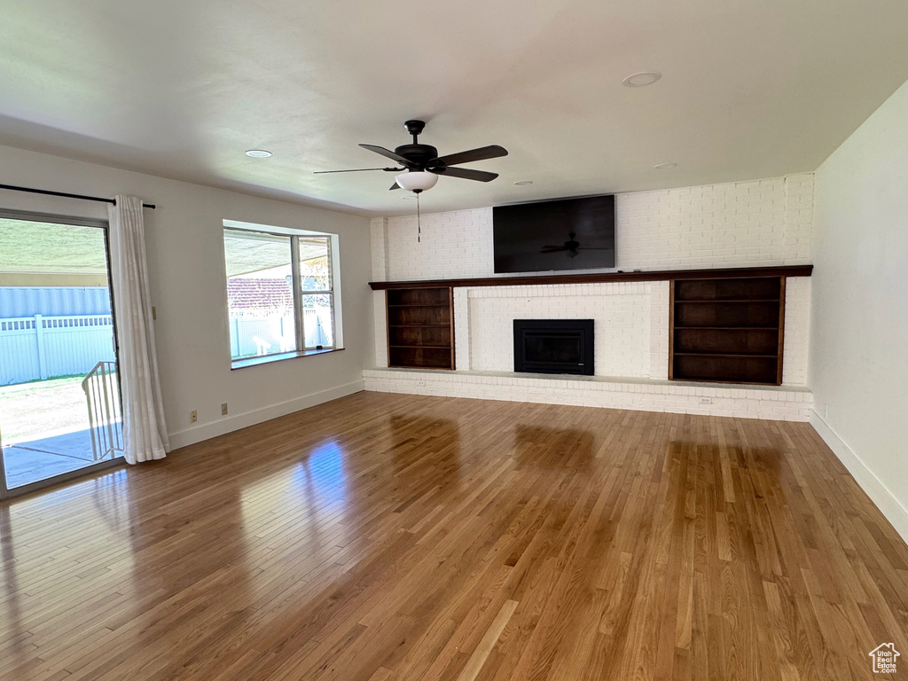 Unfurnished living room with baseboards, a brick fireplace, ceiling fan, and wood finished floors