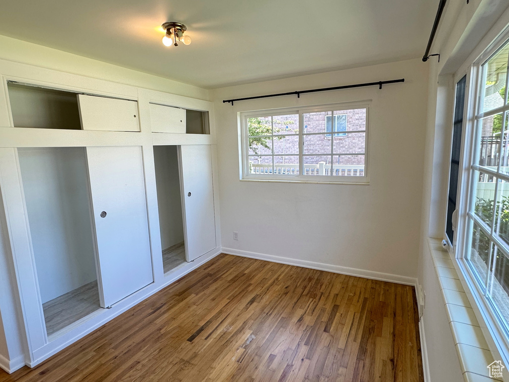 Unfurnished bedroom with multiple windows, a closet, wood finished floors, and baseboards