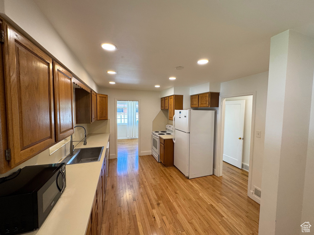 Kitchen featuring white appliances, light wood-style flooring, recessed lighting, and a sink