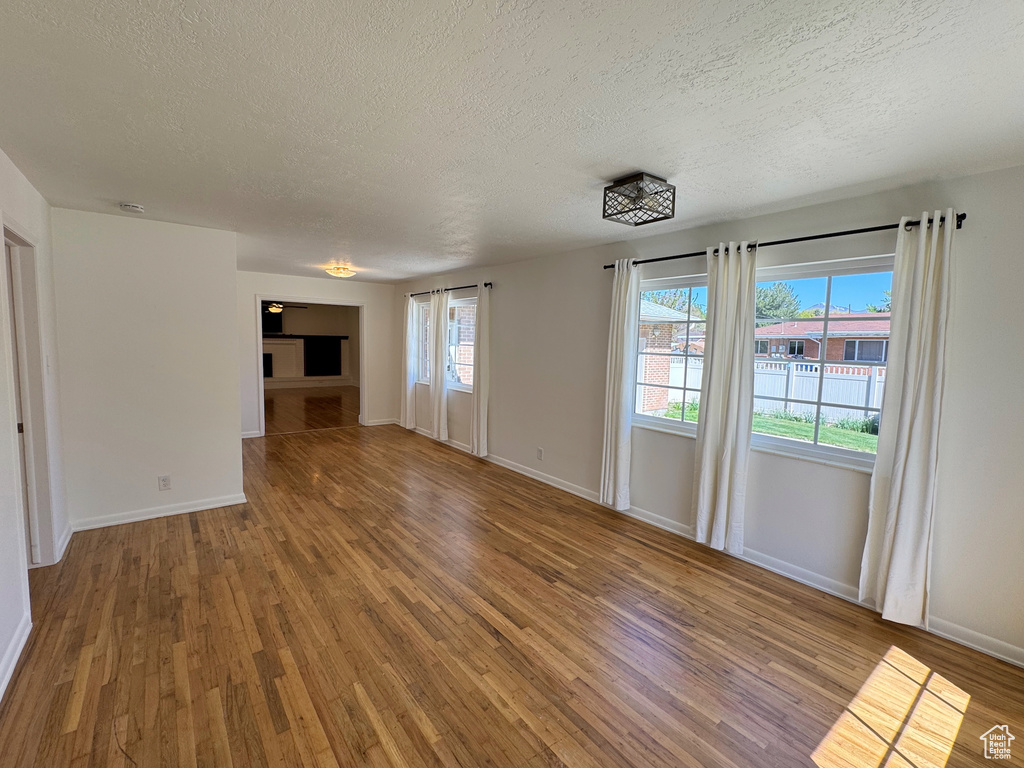 Unfurnished living room with a textured ceiling, wood finished floors, and baseboards
