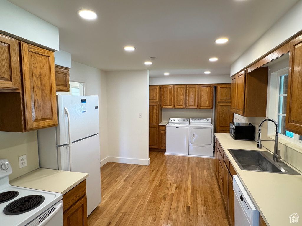 Kitchen with a sink, washer and clothes dryer, white appliances, and brown cabinets