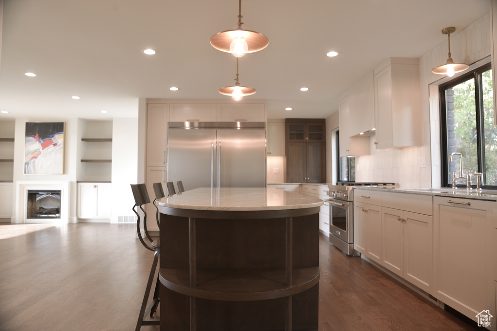 Kitchen featuring recessed lighting, premium appliances, light stone counters, hanging light fixtures, and dark wood-type flooring
