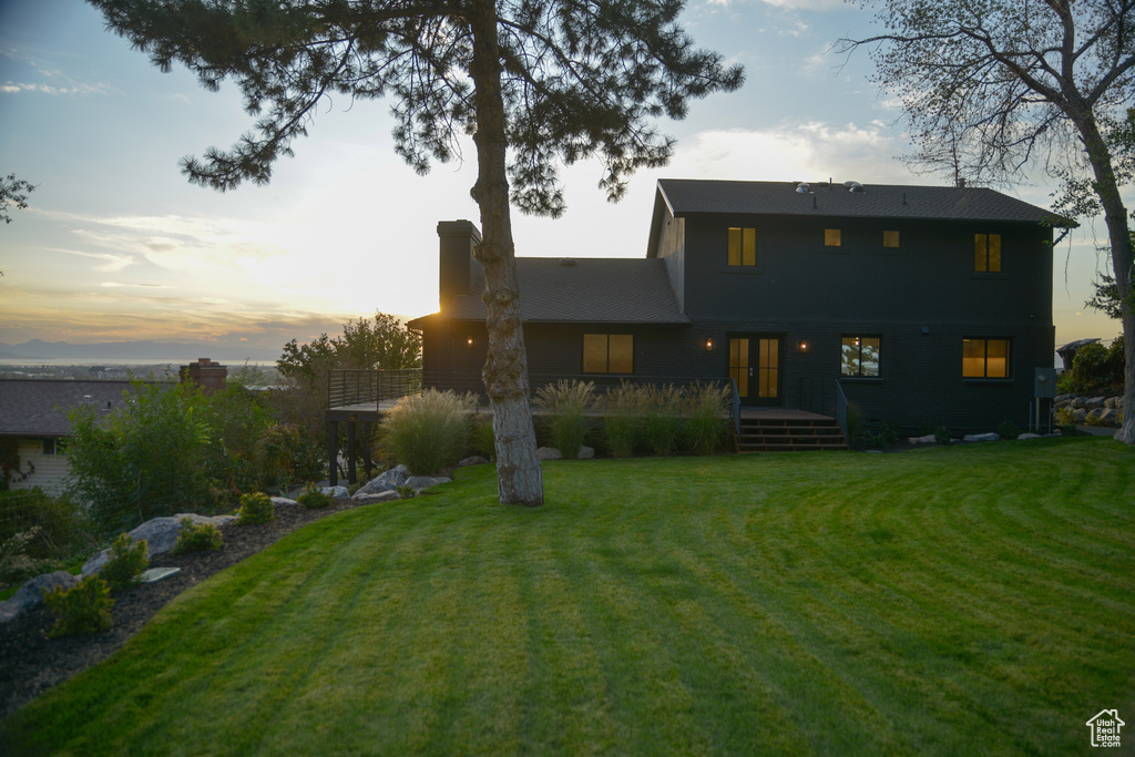 Back of house at dusk featuring a wooden deck, french doors, and a lawn