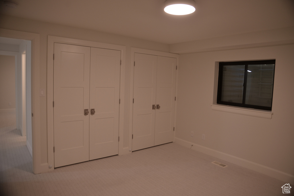 Unfurnished bedroom with carpet, visible vents, baseboards, and multiple closets