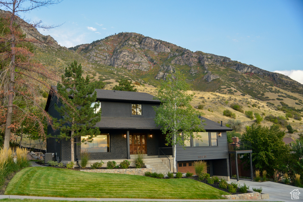 View of front facade with concrete driveway, cooling unit, a front lawn, and a mountain view
