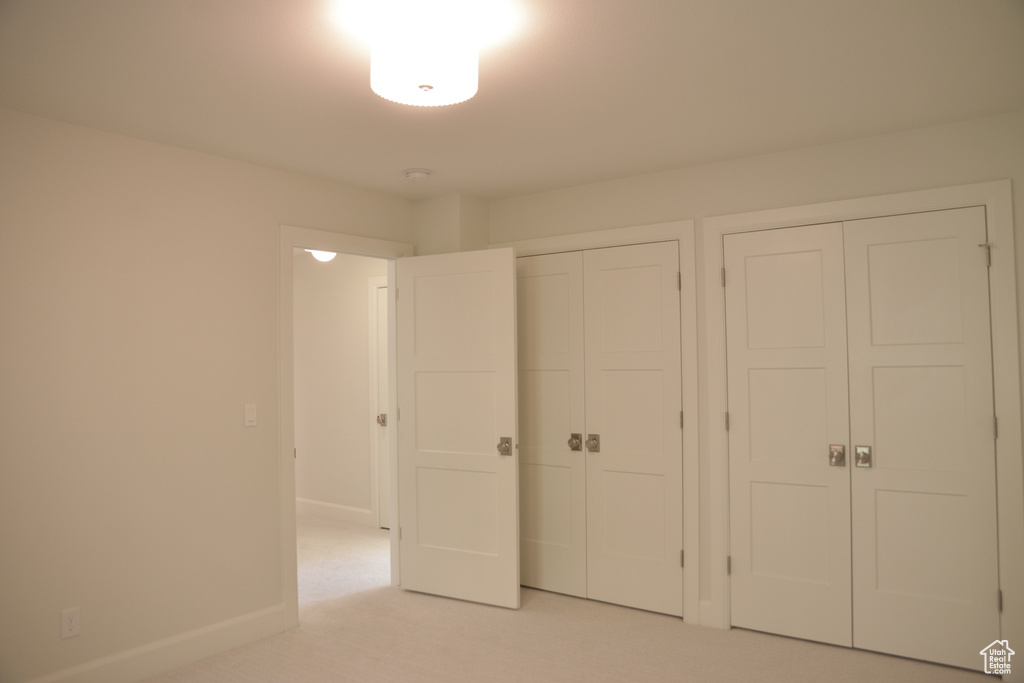 Unfurnished bedroom featuring two closets, light carpet, and baseboards