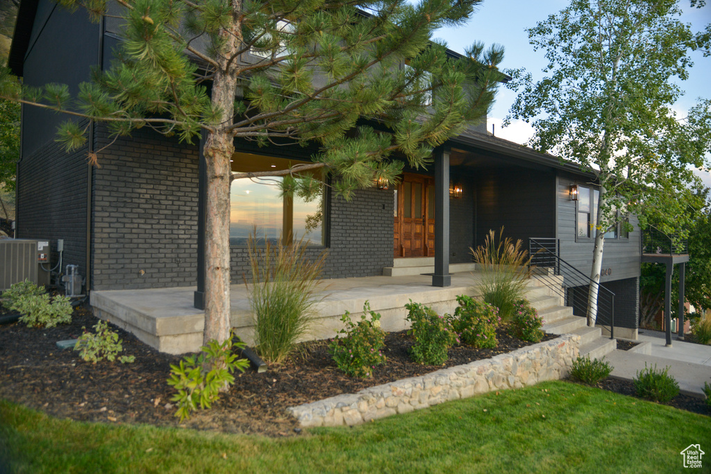 View of front facade with a porch, central air condition unit, and brick siding