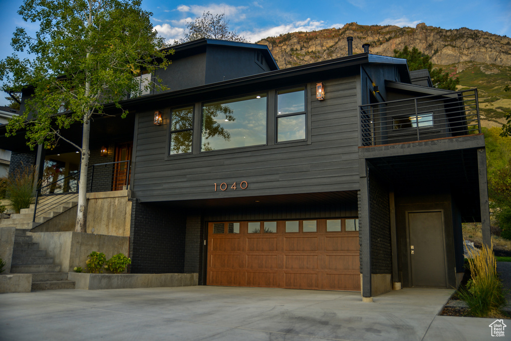 Modern home featuring an attached garage, brick siding, a balcony, concrete driveway, and stairway