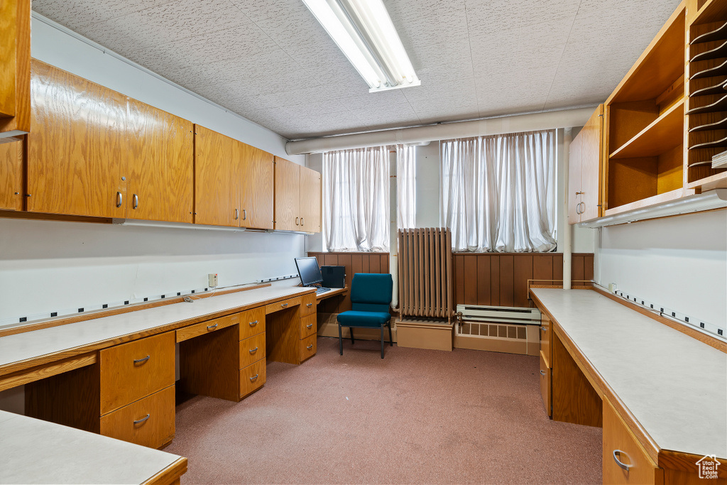 Office space featuring built in study area, light colored carpet, and a baseboard radiator