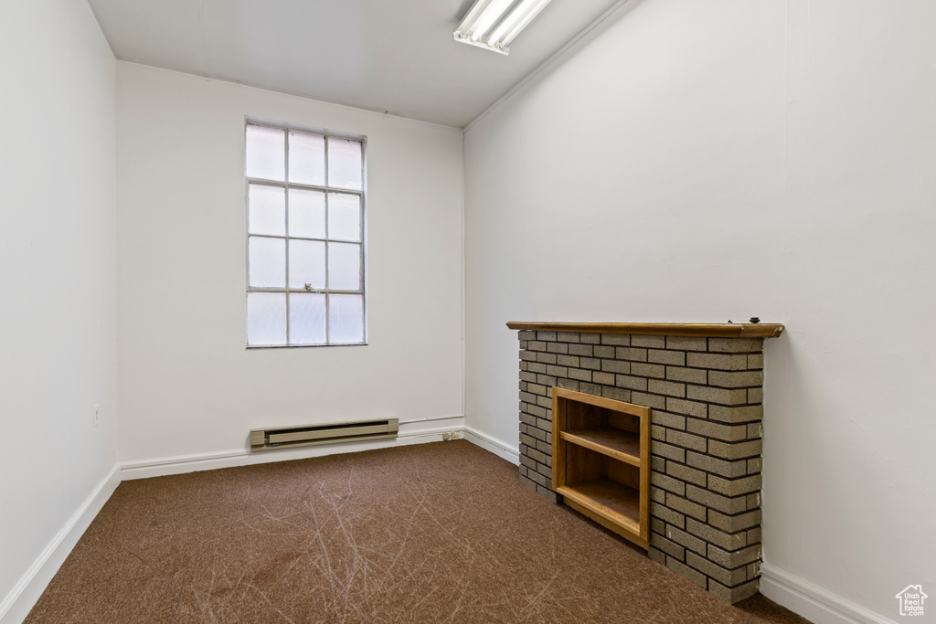 Unfurnished living room featuring dark carpet, a fireplace, a baseboard heating unit, and baseboards