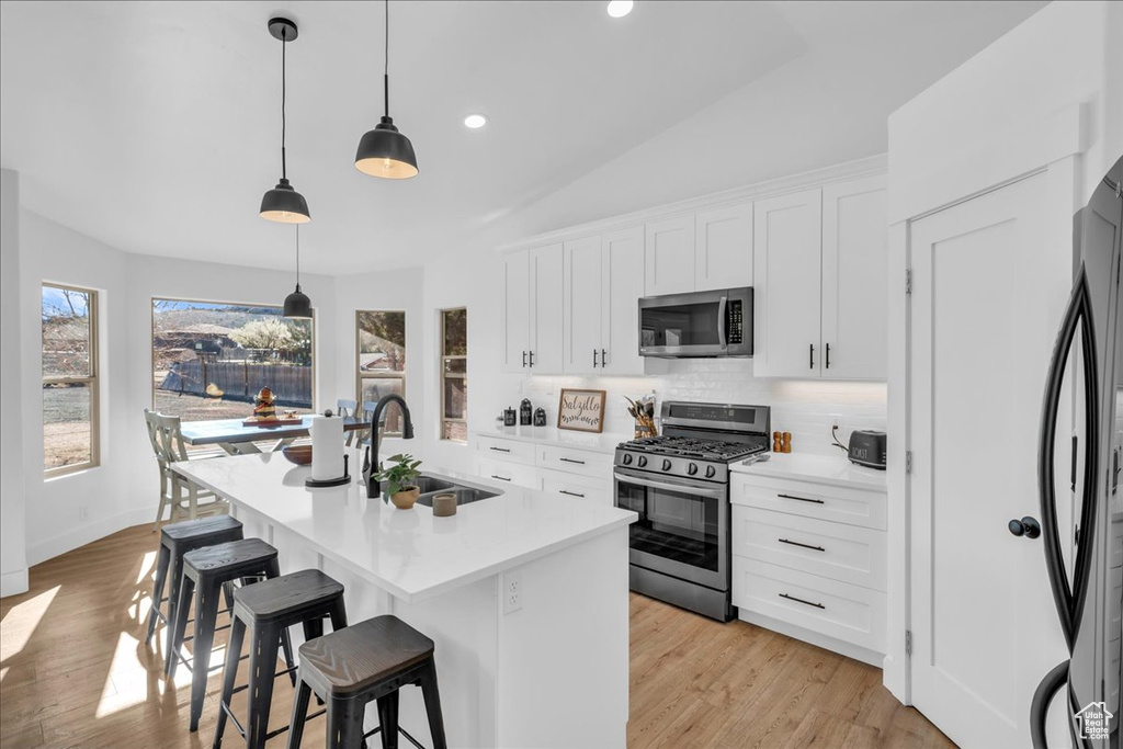 Kitchen featuring a breakfast bar area, a wealth of natural light, a sink, backsplash, and appliances with stainless steel finishes