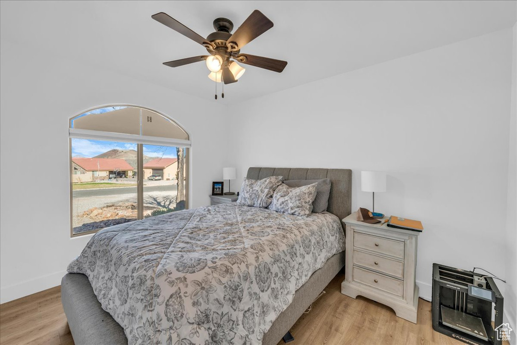 Bedroom with light wood-type flooring, baseboards, heating unit, and a ceiling fan