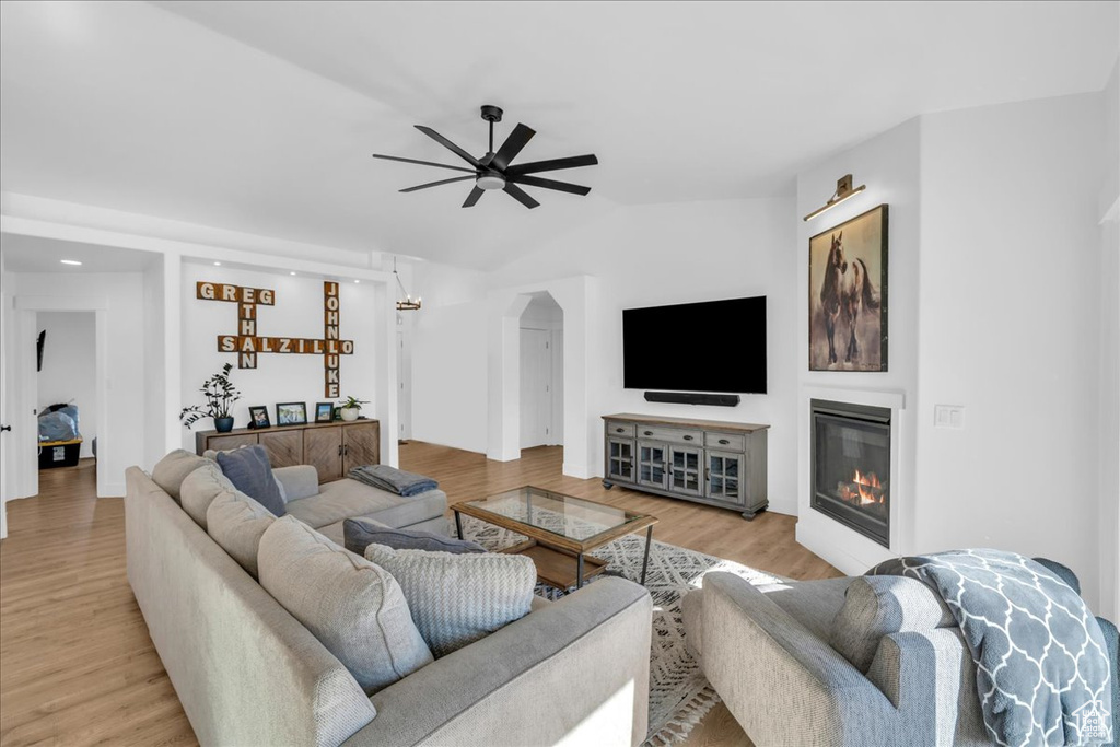 Living room with a ceiling fan, arched walkways, a glass covered fireplace, light wood-style floors, and vaulted ceiling
