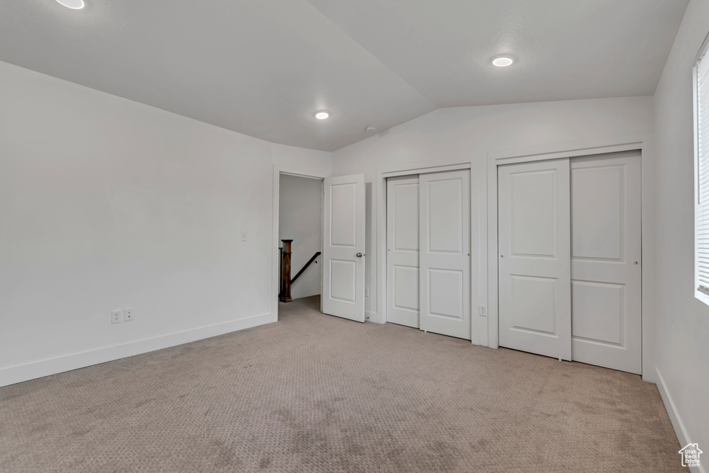 Unfurnished bedroom featuring carpet flooring, vaulted ceiling, baseboards, and multiple closets