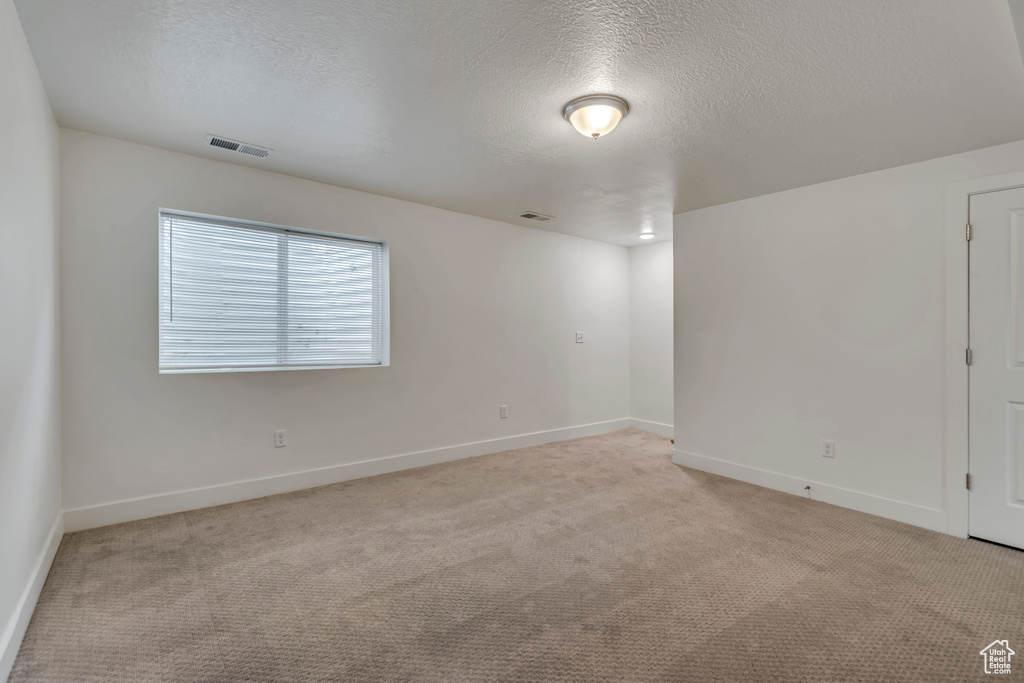 Spare room with light carpet, a textured ceiling, baseboards, and visible vents