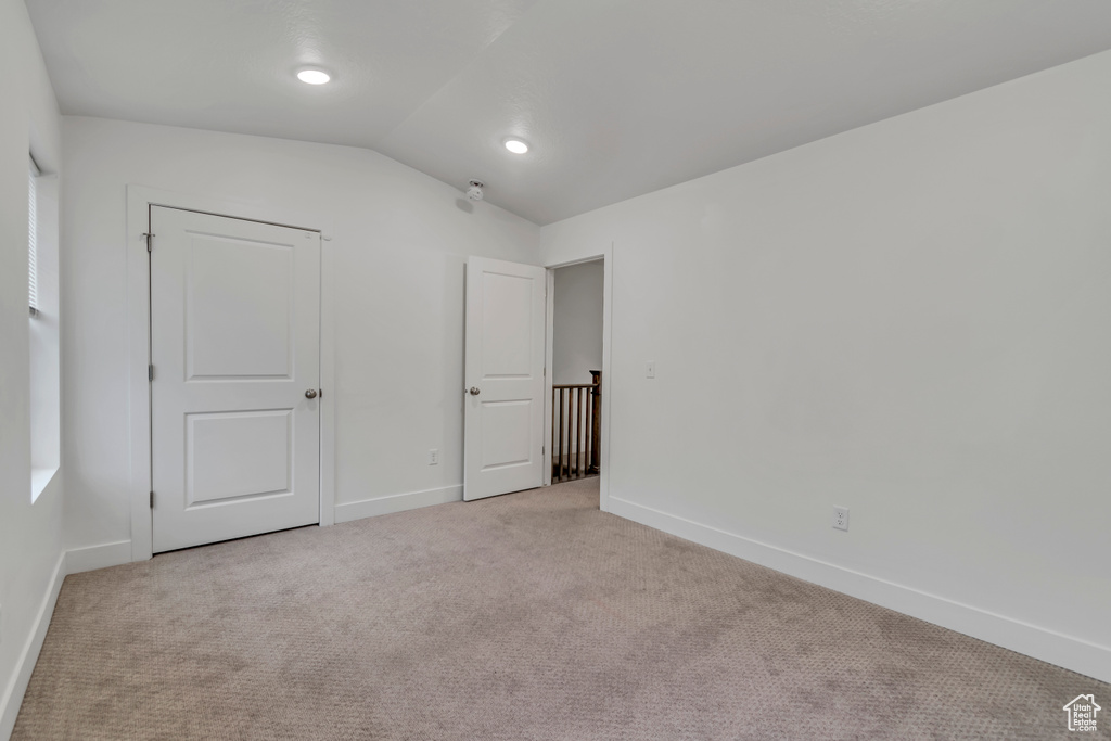 Unfurnished bedroom featuring vaulted ceiling, light carpet, and baseboards