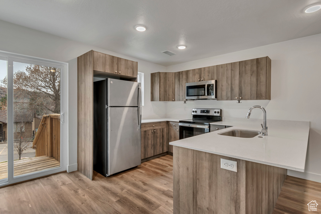Kitchen with a peninsula, a sink, brown cabinetry, light countertops, and appliances with stainless steel finishes