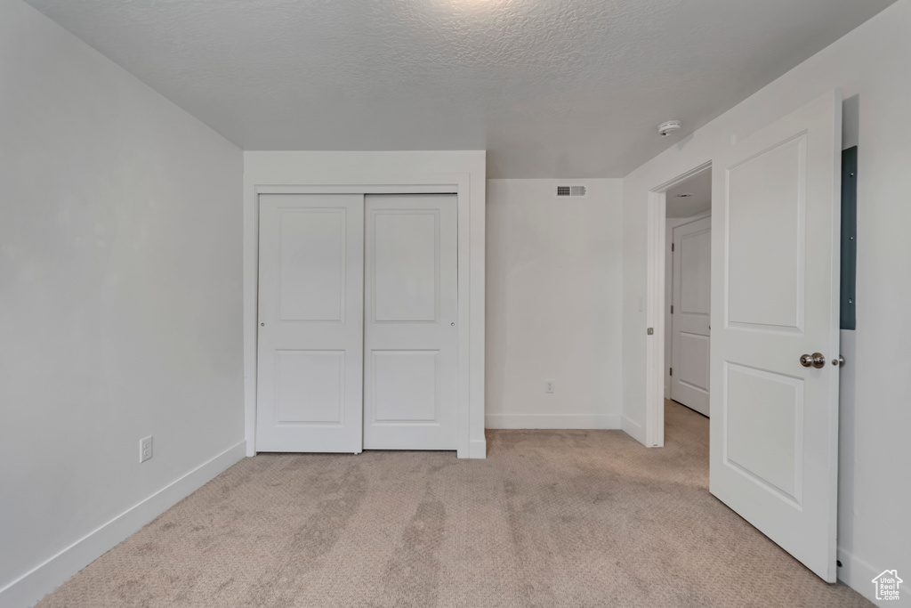 Unfurnished bedroom featuring a closet, a textured ceiling, visible vents, light carpet, and baseboards