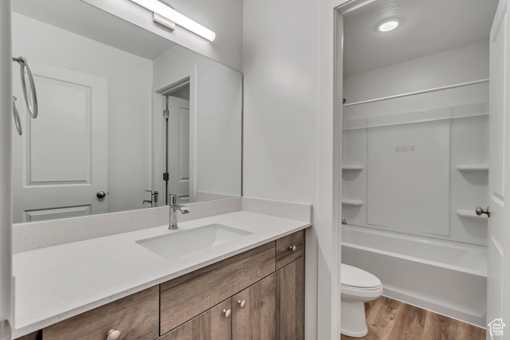Full bath with shower / bath combination, vanity, toilet, and wood finished floors