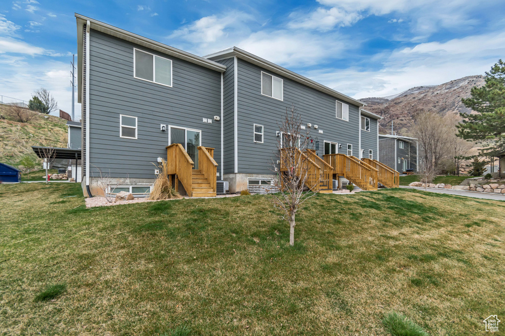 Back of house with a mountain view, a lawn, and central AC