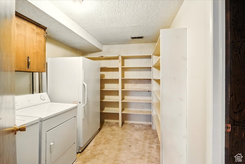 Laundry room featuring washer and clothes dryer, cabinet space, a textured ceiling, visible vents, and light carpet