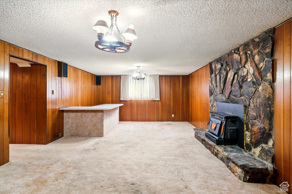 Unfurnished living room featuring carpet floors, a textured ceiling, wood walls, a wood stove, and a chandelier