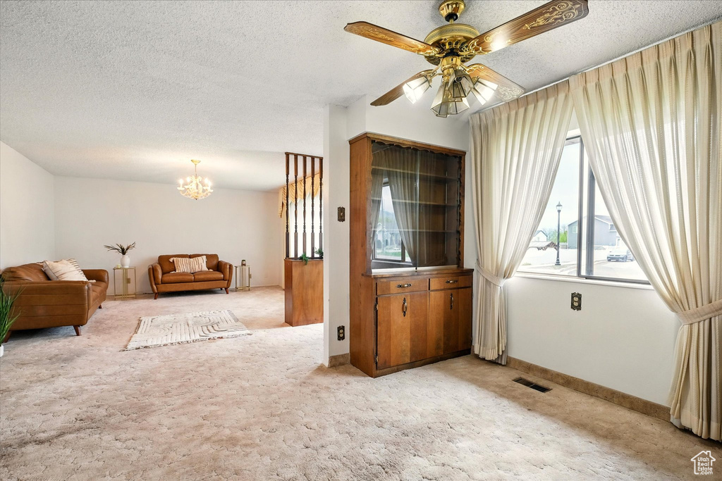 Living room with a textured ceiling, visible vents, light colored carpet, and ceiling fan with notable chandelier