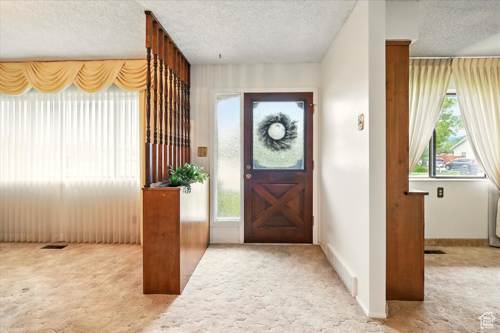 Carpeted entrance foyer featuring a wealth of natural light, visible vents, and a textured ceiling