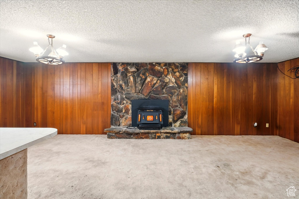 Unfurnished living room featuring carpet flooring, wood walls, a chandelier, and a wood stove