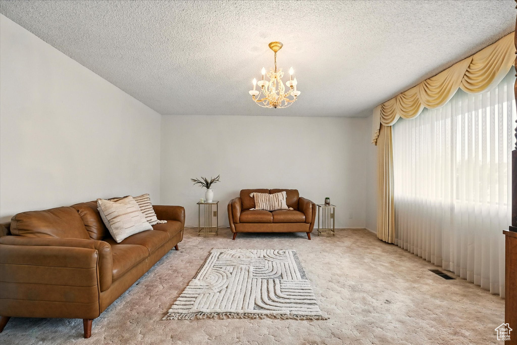 Living room featuring light colored carpet, a textured ceiling, a notable chandelier, and visible vents