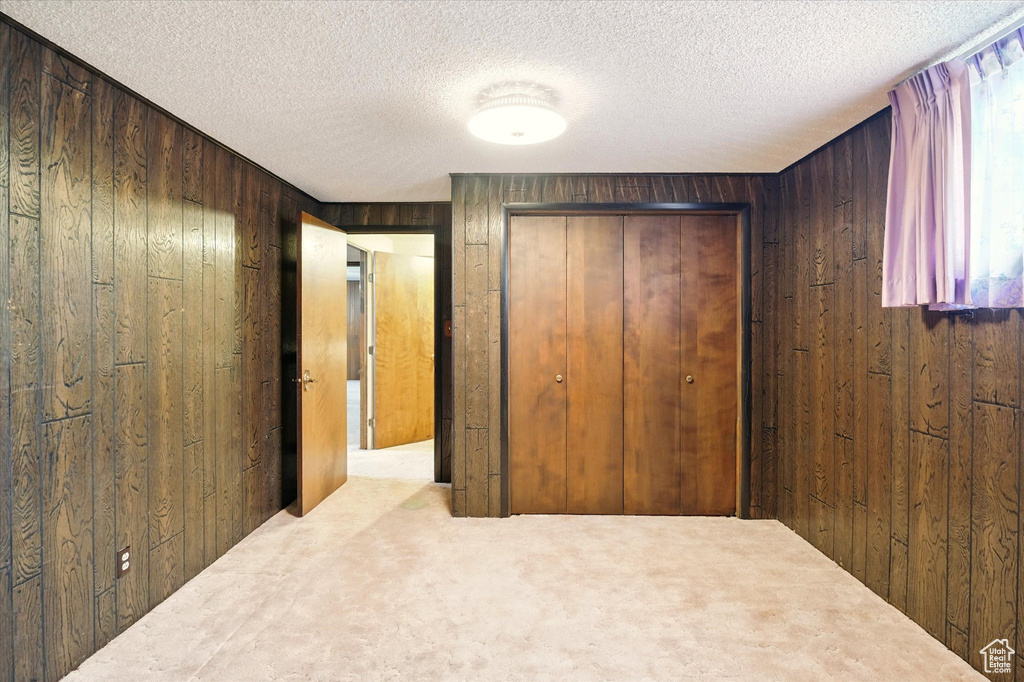 Unfurnished bedroom featuring a closet, a textured ceiling, wooden walls, and carpet floors