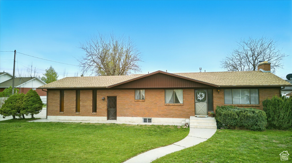 Single story home featuring a chimney, a front yard, roof with shingles, and brick siding