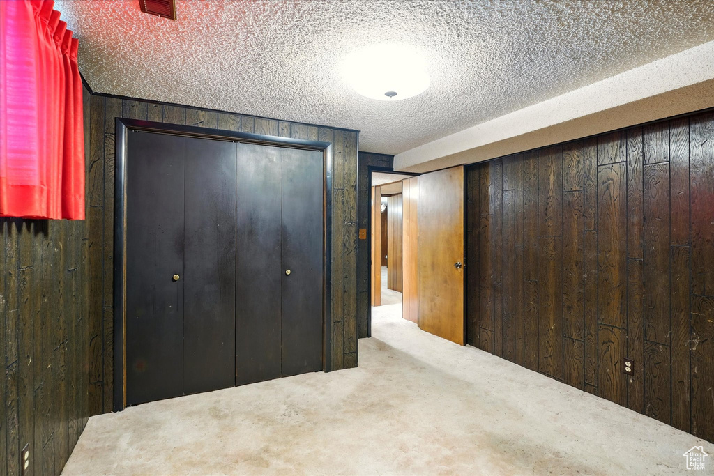 Unfurnished bedroom featuring a textured ceiling, wood walls, visible vents, and carpet