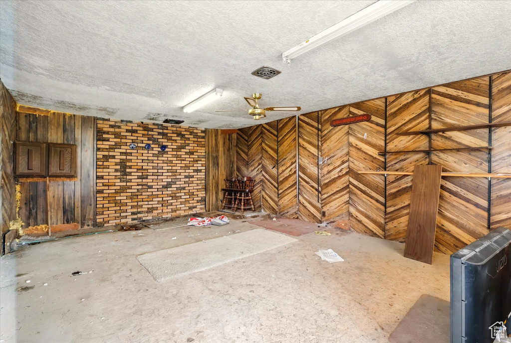 Interior space with a textured ceiling, wooden walls, and a ceiling fan