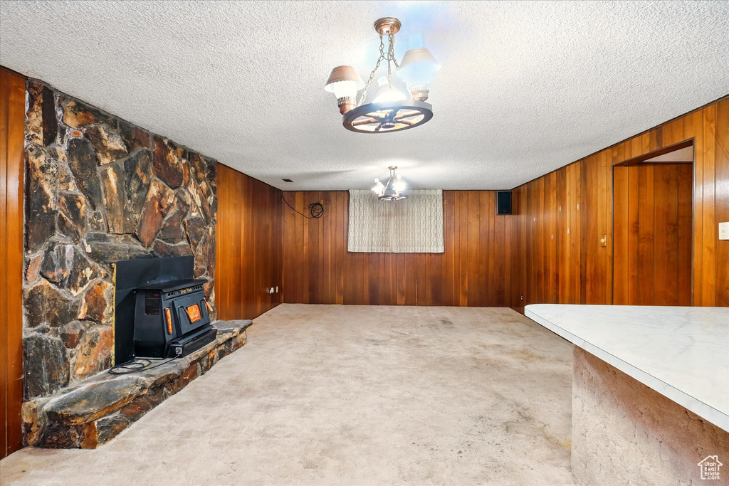 Carpeted living area with a wood stove, an inviting chandelier, a textured ceiling, and wood walls