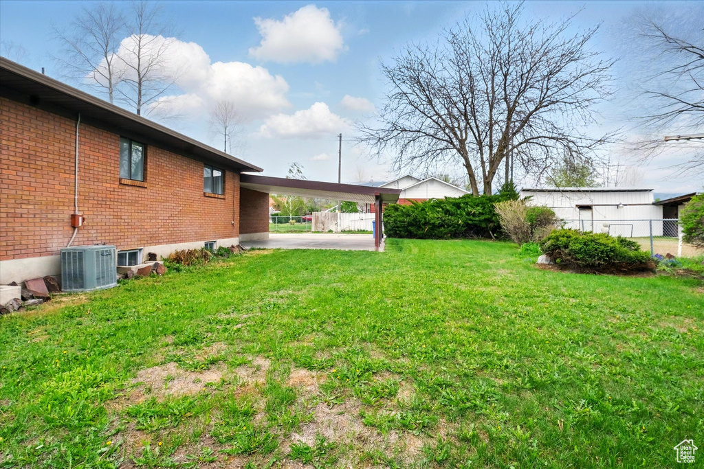 View of yard with central AC unit, fence, and a carport