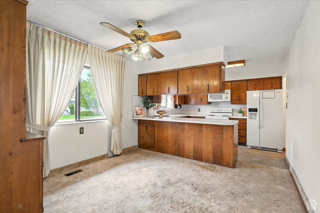 Kitchen with a peninsula, brown cabinetry, white appliances, visible vents, and baseboards